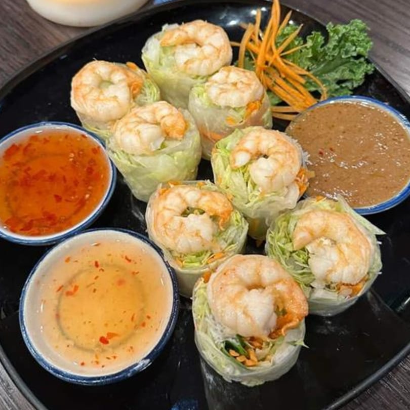 Eight fresh shrimp spring rolls with lettuce, carrots, and two dipping sauces on a black plate.