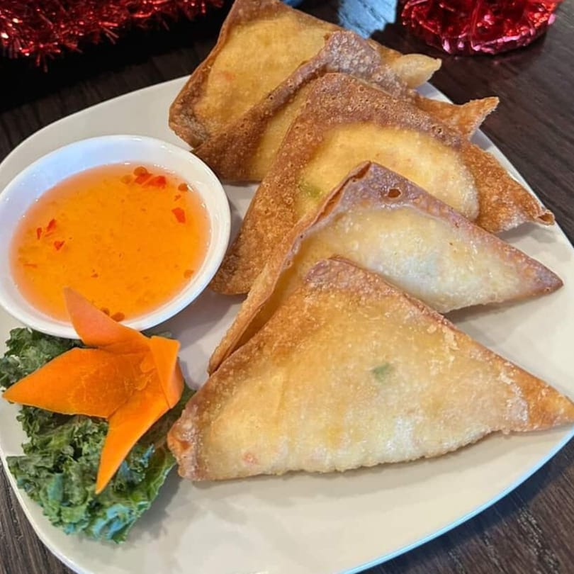 Golden-brown fried wontons arranged on a white plate with a side of orange dipping sauce.