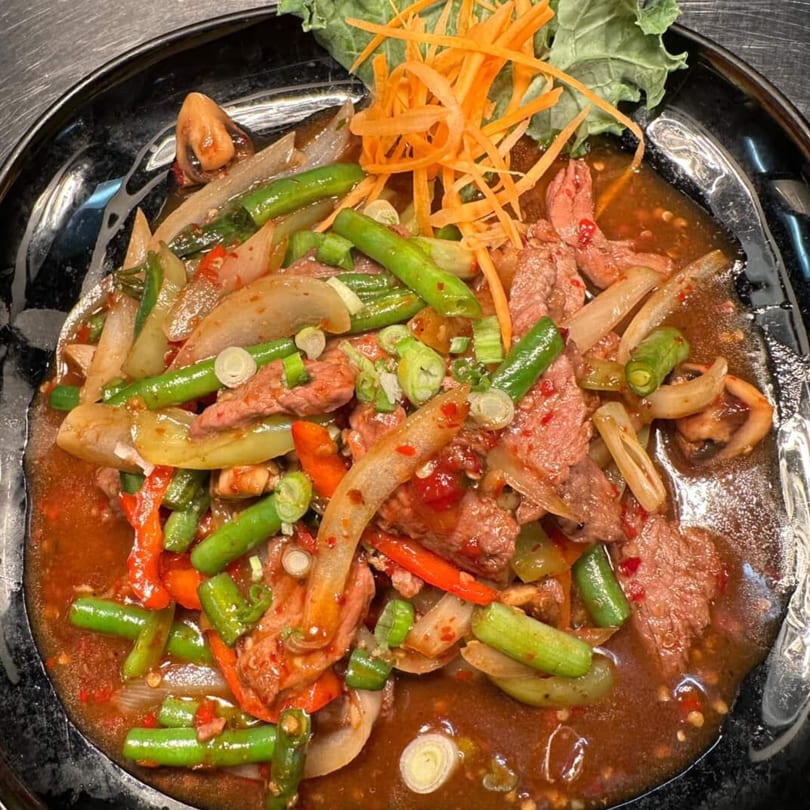 Spicy beef stir-fry with green beans, onions, and red peppers, garnished with shredded carrots.